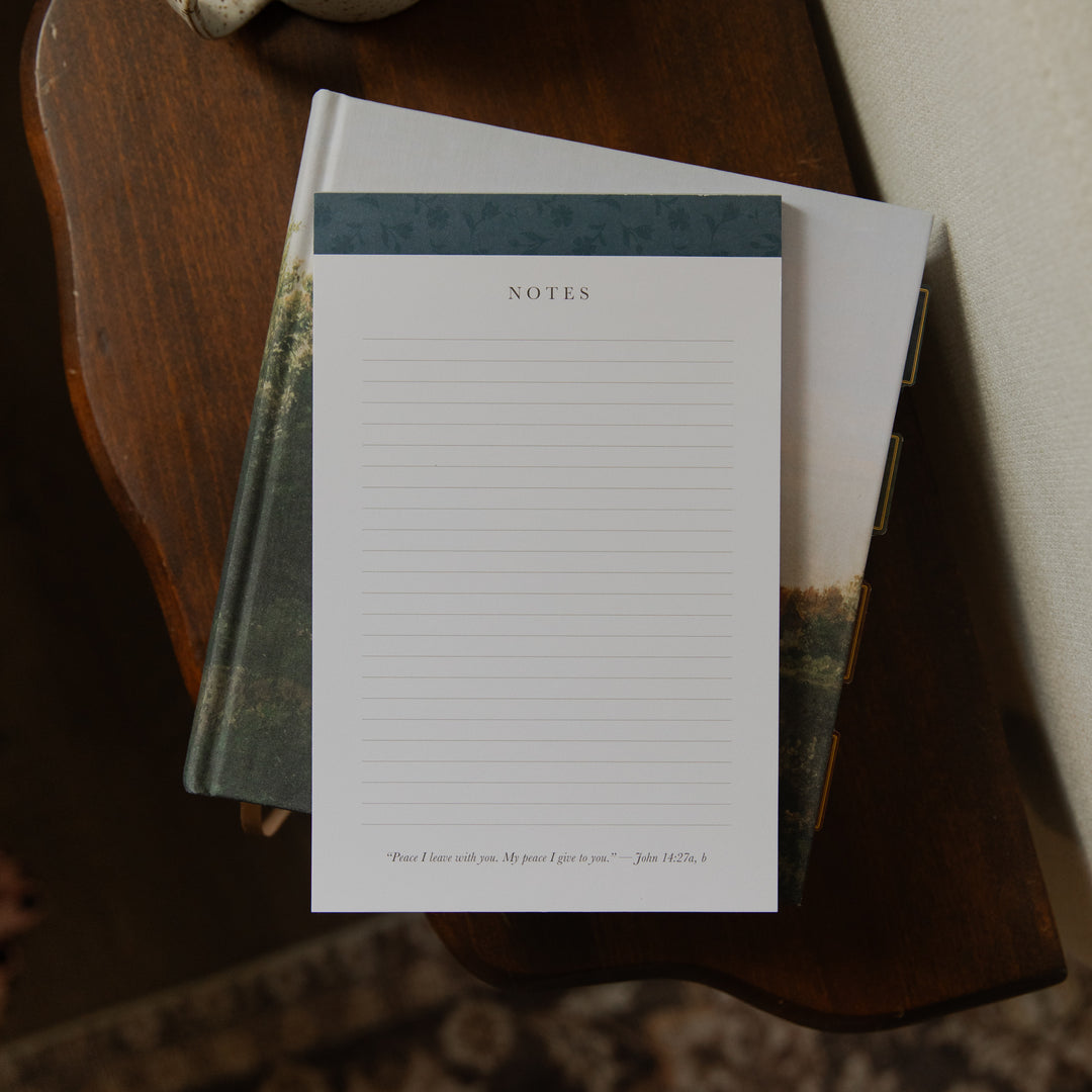 A floral notepad on a closed bible on a wooden table