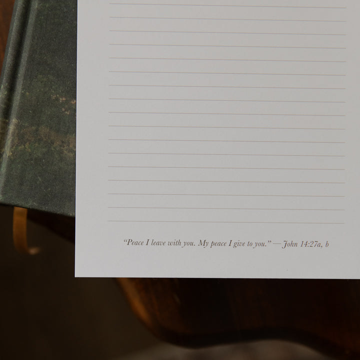 Up close of the bottom of A floral notepad on a closed bible on a wooden table