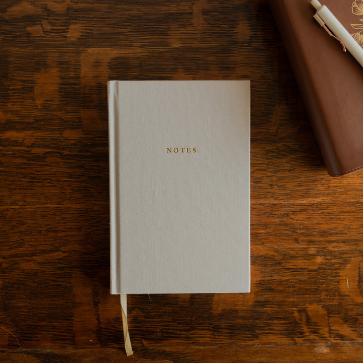 The Notes Lined Journal cover on a wooden table next to a bible with a white pen on it