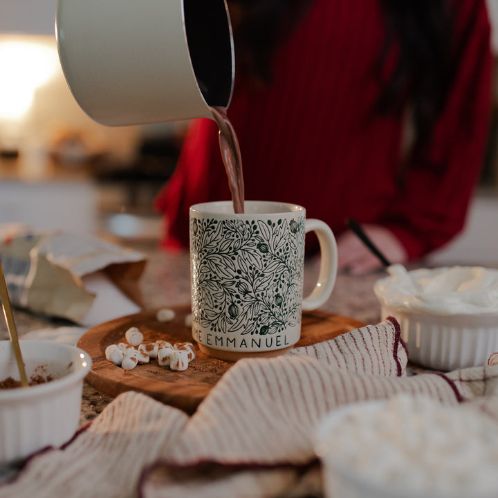 A woman pouring hot chocolate into the O Come O Come Emmanuel mug resting on a rotating wooden round wheel