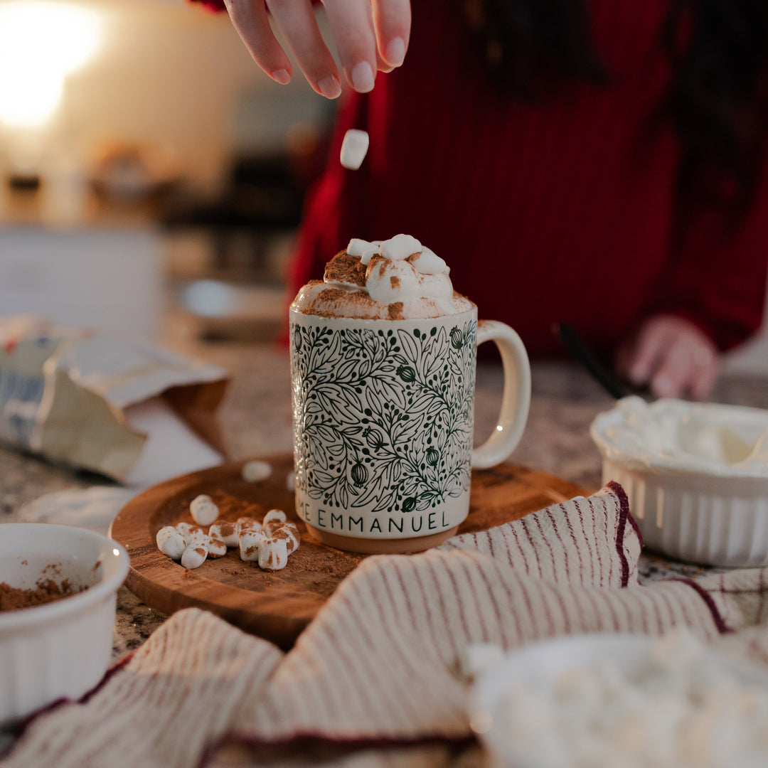 A woman dropping marshmallows into the O Come O Come Emmanuel mug resting on a rotating wooden round wheel