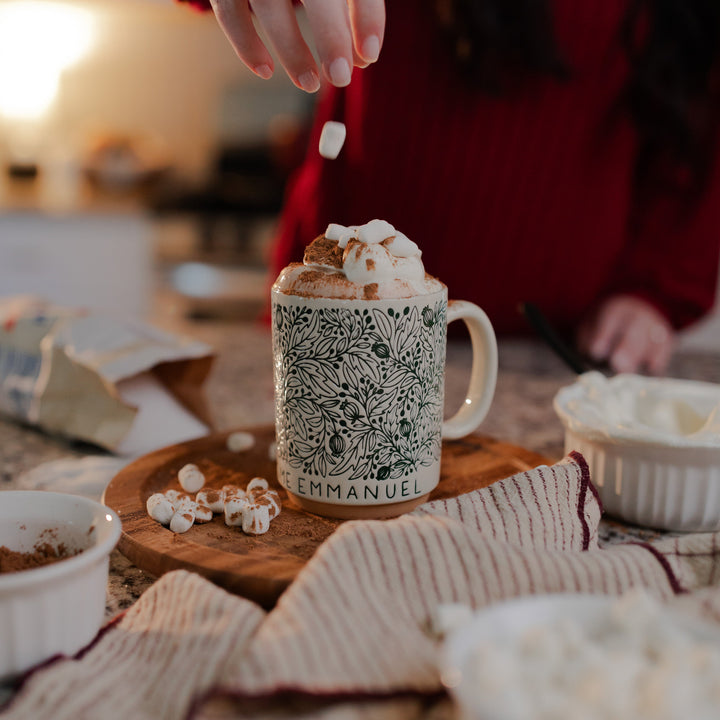 A woman dropping marshmallows into the O Come O Come Emmanuel mug resting on a rotating wooden round wheel