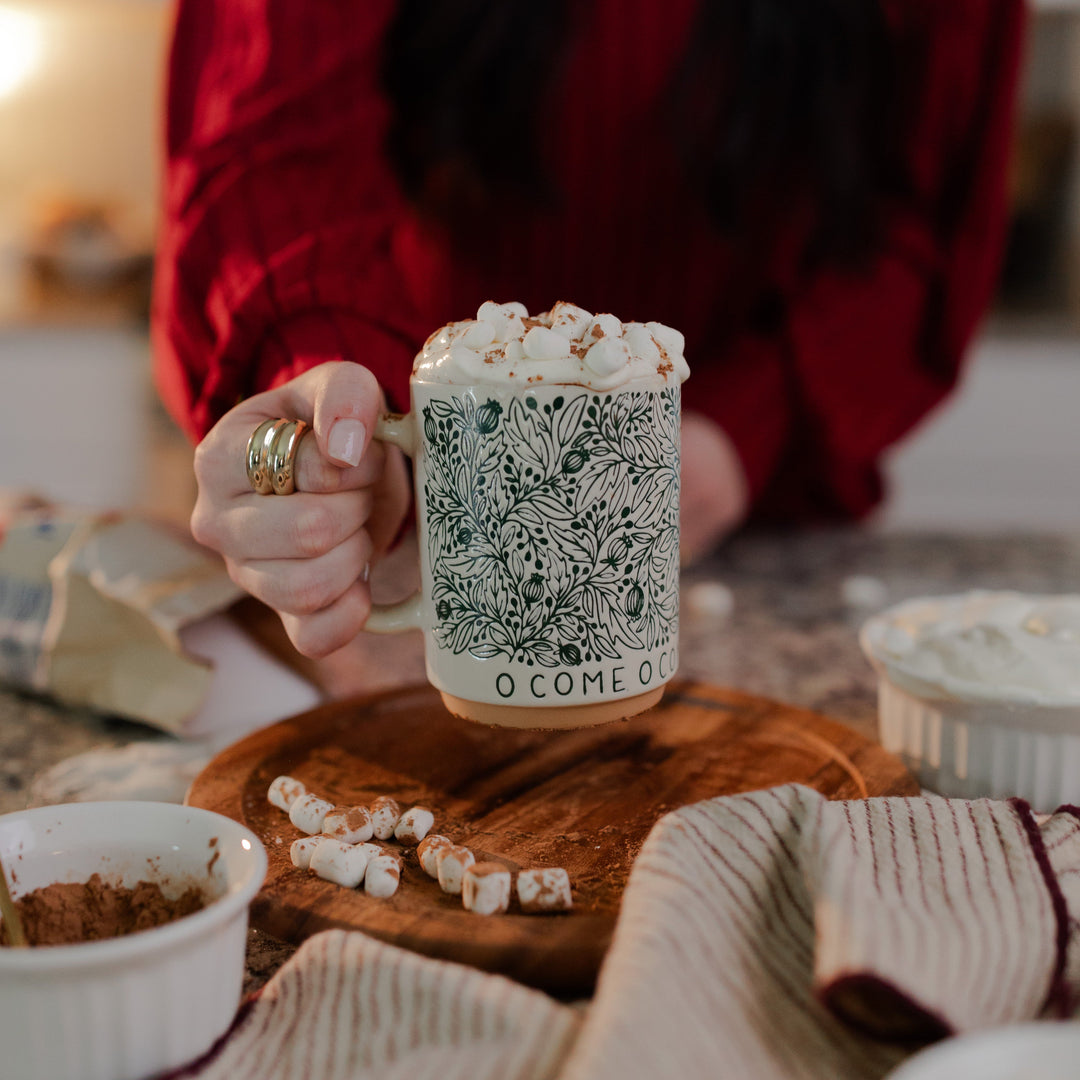 A woman holding the handle of the O Come O Come Emmanuel mug resting on a rotating wooden round wheel