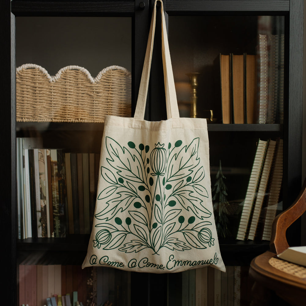 O Come O Come Emmanuel Tote on a black wooden bookshelf with various books on it