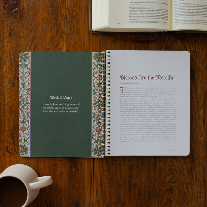Open notebook with decorative binding on a wooden surface, next to an open book and a mug.