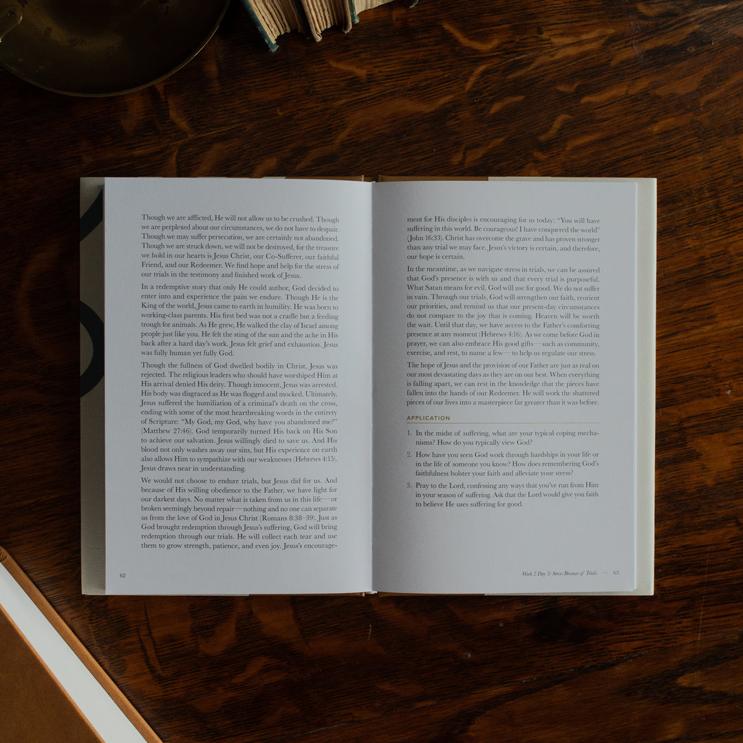 Peace Under Pressure Mens opened to the Week 2 reading page on a wooden table next to a journal