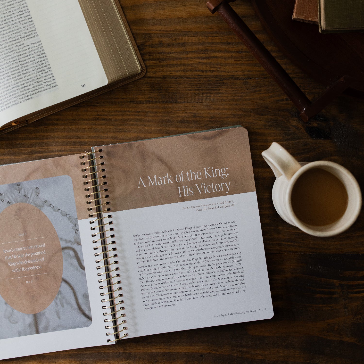 Peaks and Valleys Spiral Study opened to the mark of the king page next to a dark brown wooden tray and an open bible and a white coffee cup on a brown wooden table