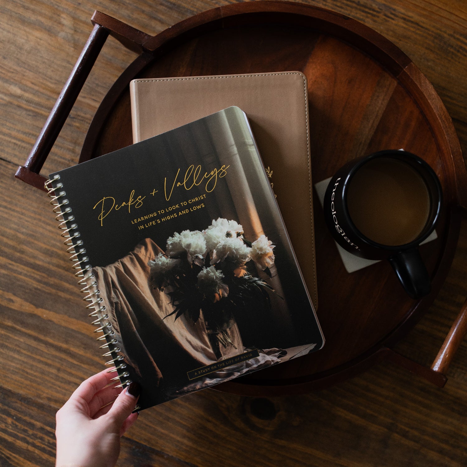 Peaks and Valleys Spiral Study on a dark brown wooden tray as a woman holds a corner of the study with a black coffee cup next to it on a brown wooden table
