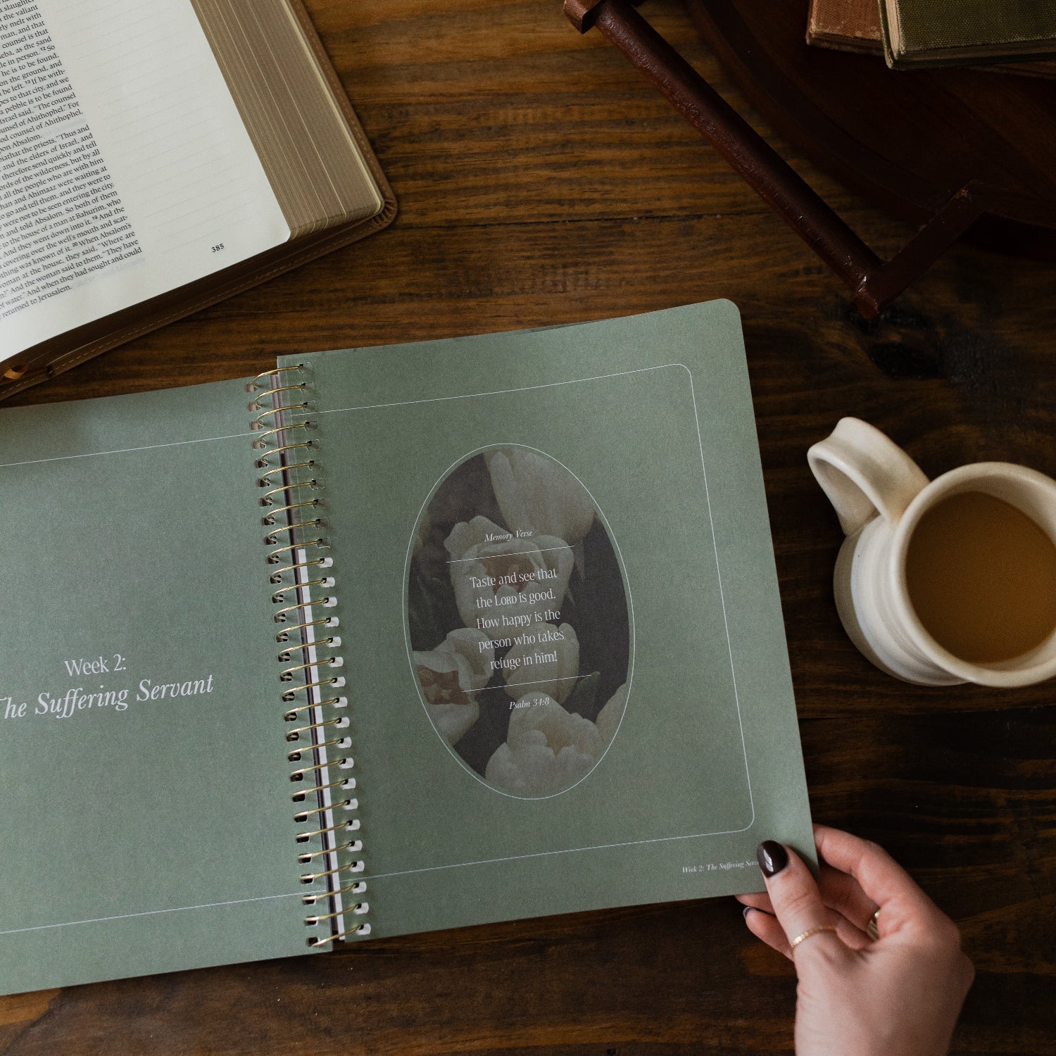 Peaks and Valleys Spiral Study opened to memory verse for Psalms with a woman's hand holding the corner next to a dark brown wooden tray and an open bible and a white coffee cup on a brown wooden table
