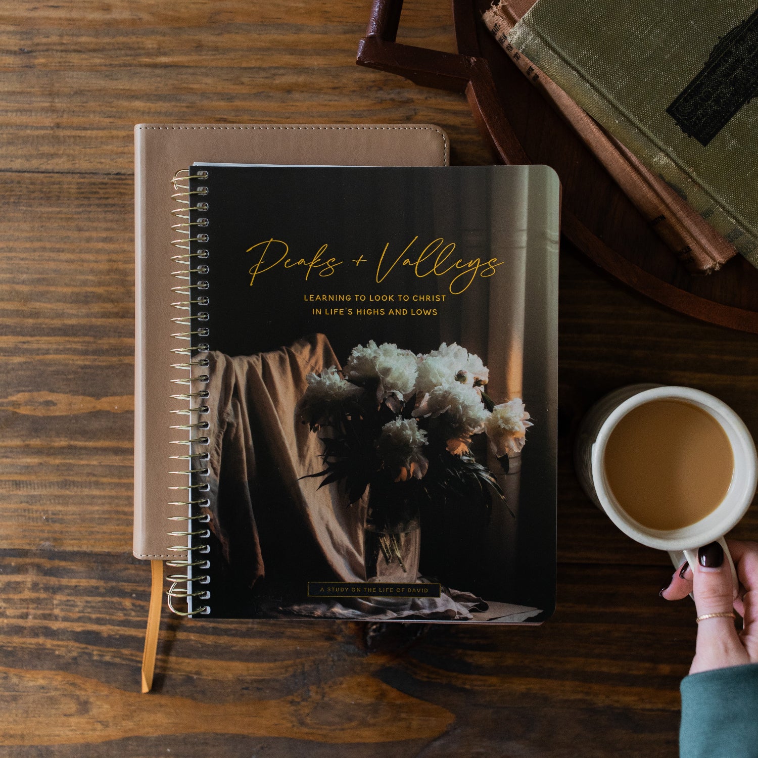 Peaks and Valleys Spiral Study next to a dark brown wooden tray with a white coffee cup with a woman's hand holding the handle next to it on a brown wooden table