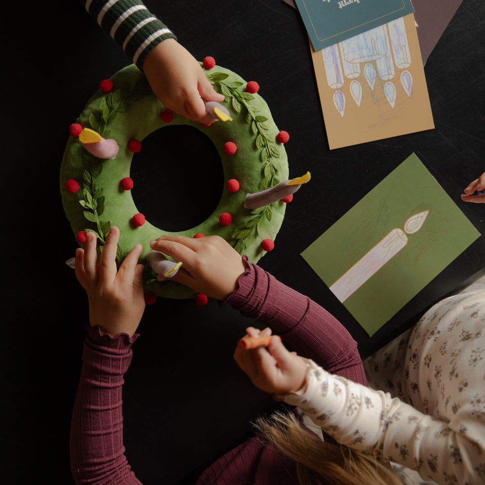 Kids touching a plush wreath on a black table near some cards