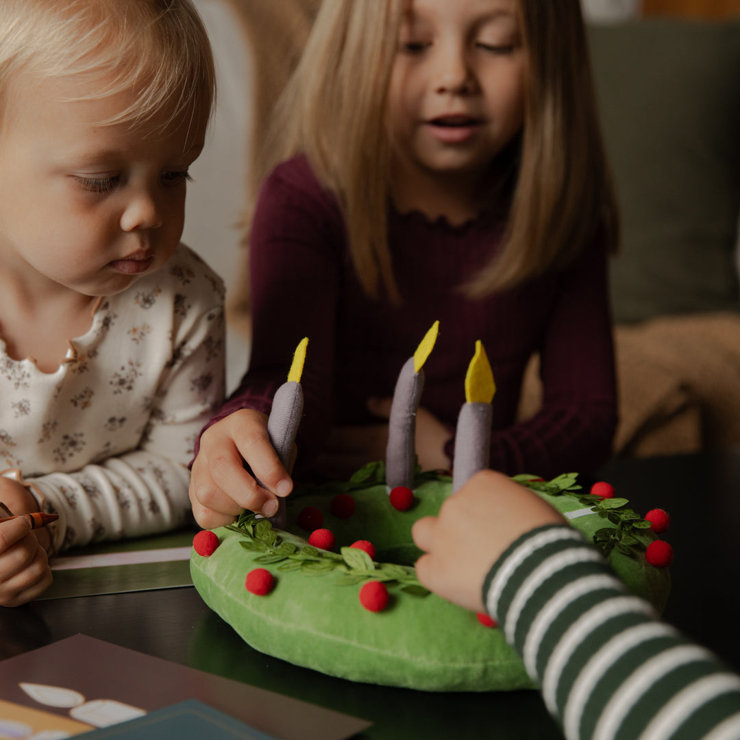 Kids touching the candles on a plush wreath on a black table