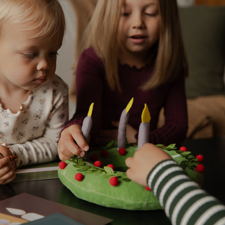 Kids touching the candles on a plush wreath on a black table