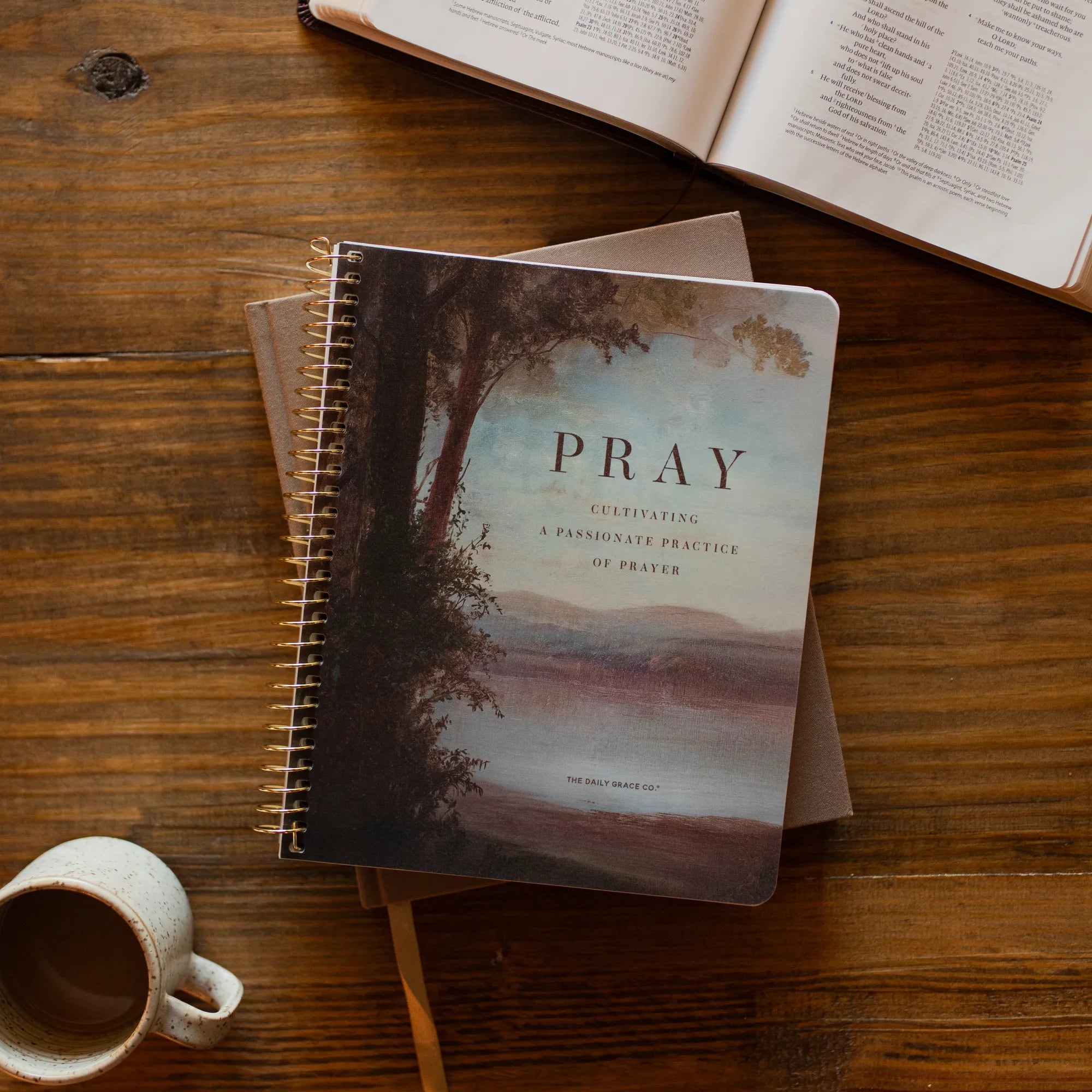 The Pray Spiral Study cover on a closed journal on a wooden table near an open bible