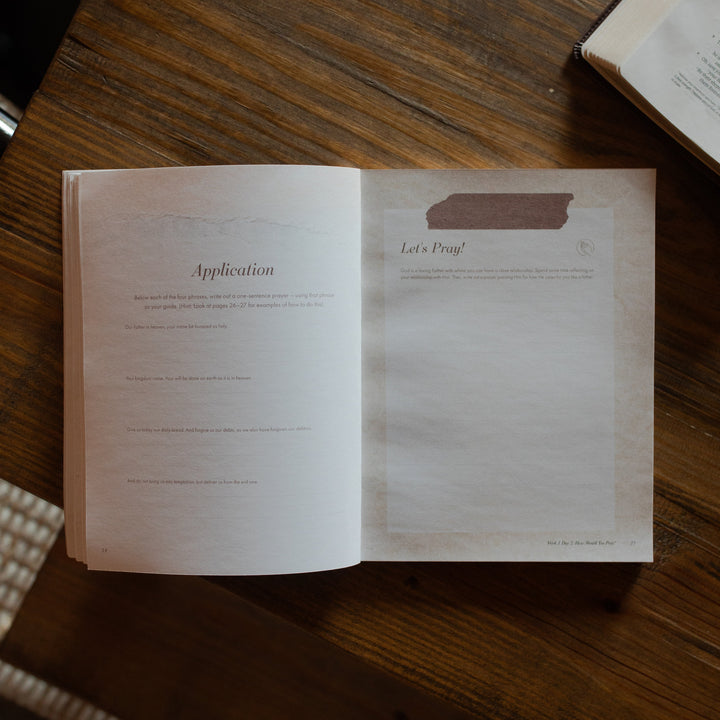 The Pray study opened to the the application and prayer page on a wooden table near an open bible