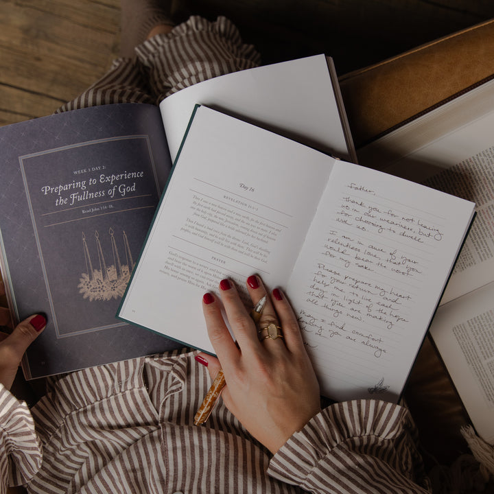 A person's hands with red nail polish and rings are shown holding open a book titled 'Preparing to Experience the Fullness of God' from the Book of Common Prayer. The scene is styled as a flat lay on a striped blanket and wooden floor.