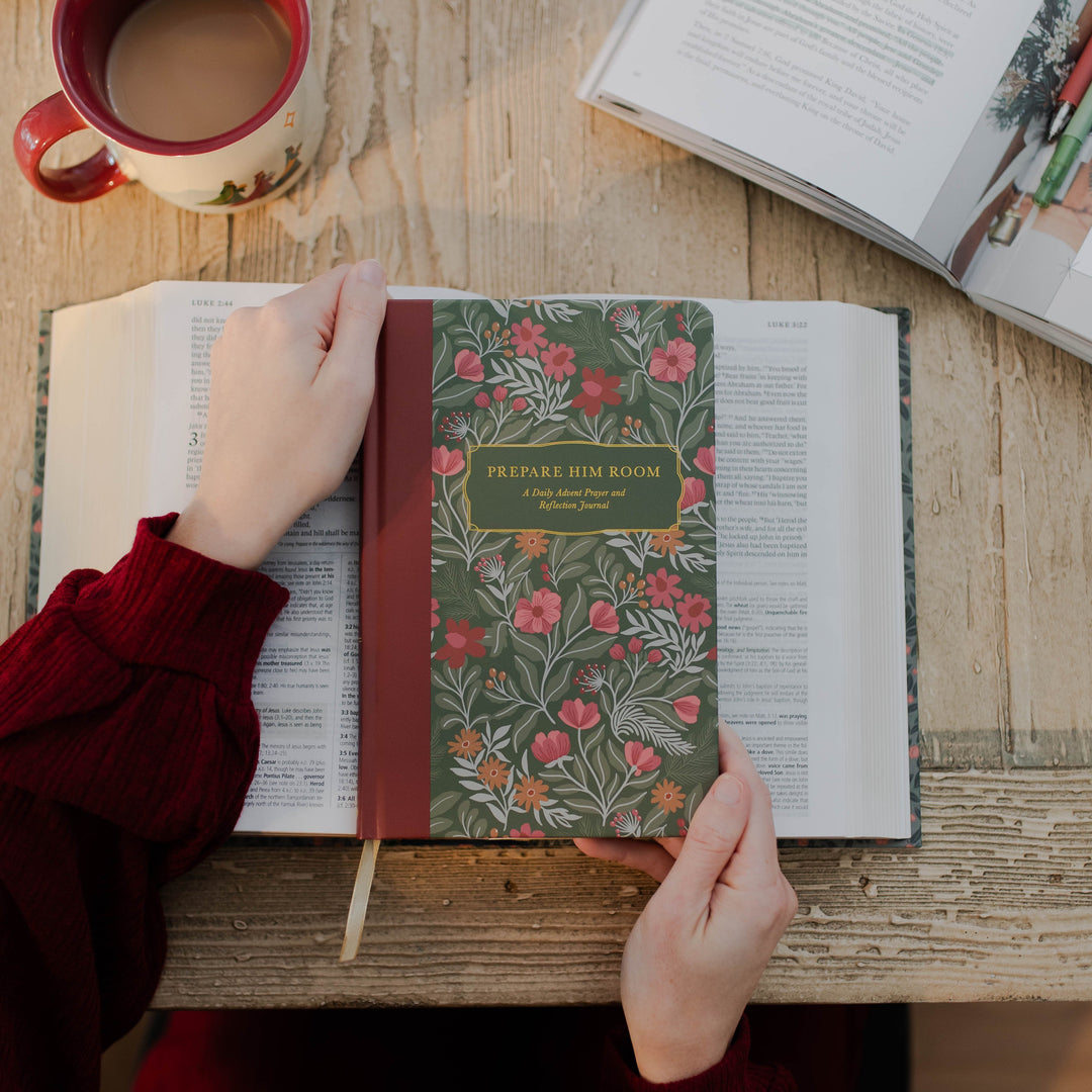 Woman holding Prepare Him Room Daily Advent Prayer and Reflection Journal over Bible