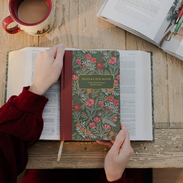 Woman holding Prepare Him Room Daily Advent Prayer and Reflection Journal over Bible