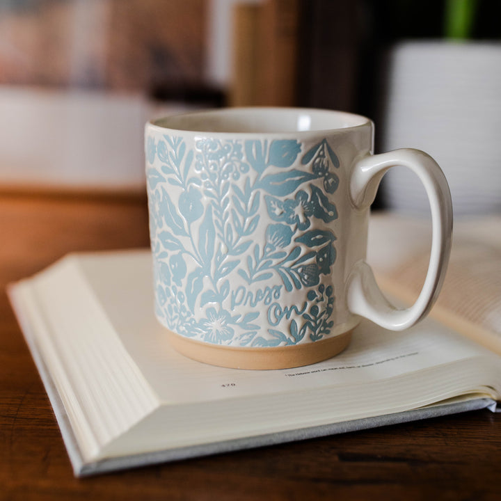 A blue and white mug with the words "press on"