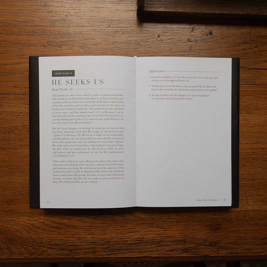 An open Bible book laid flat on a dark wooden table, showing two interior pages with printed text. The left page has the heading 'BIBLE' and the main heading 'HE SEES US' with body text below.