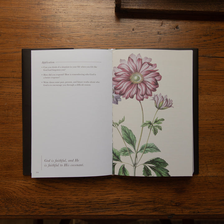 An open book lying on a wooden table, showing a printed page with text on the left and a large pink floral illustration on the right.