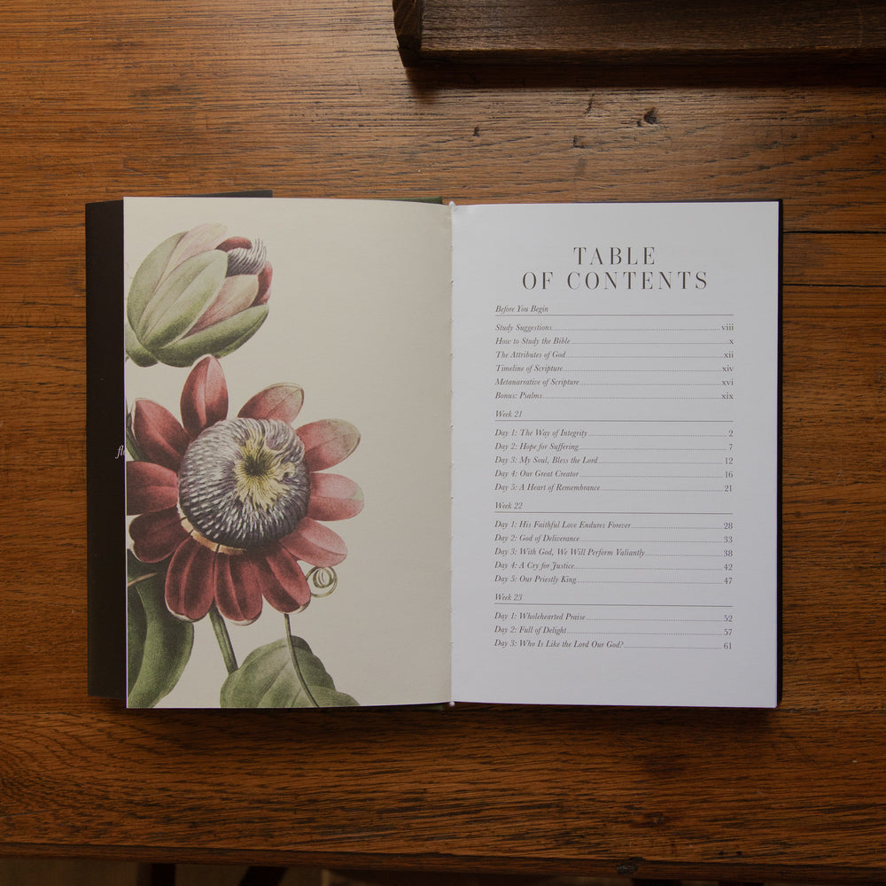 An open book laid flat on a wooden table, showing a floral illustration on the left page and a table of contents on the right page.