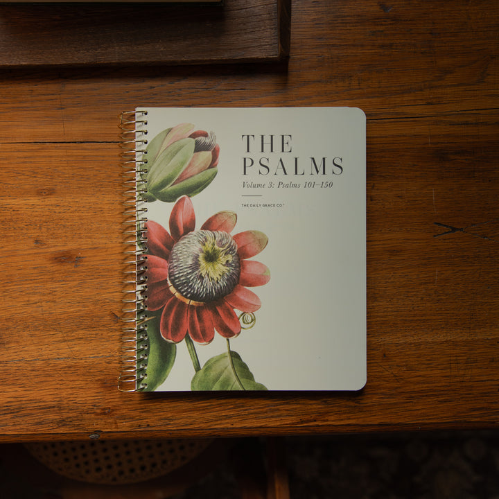 A spiral-bound book titled 'THE PSALMS Volume 3: Psalms 101-150' with a botanical cover illustration, placed on a wooden tabletop.