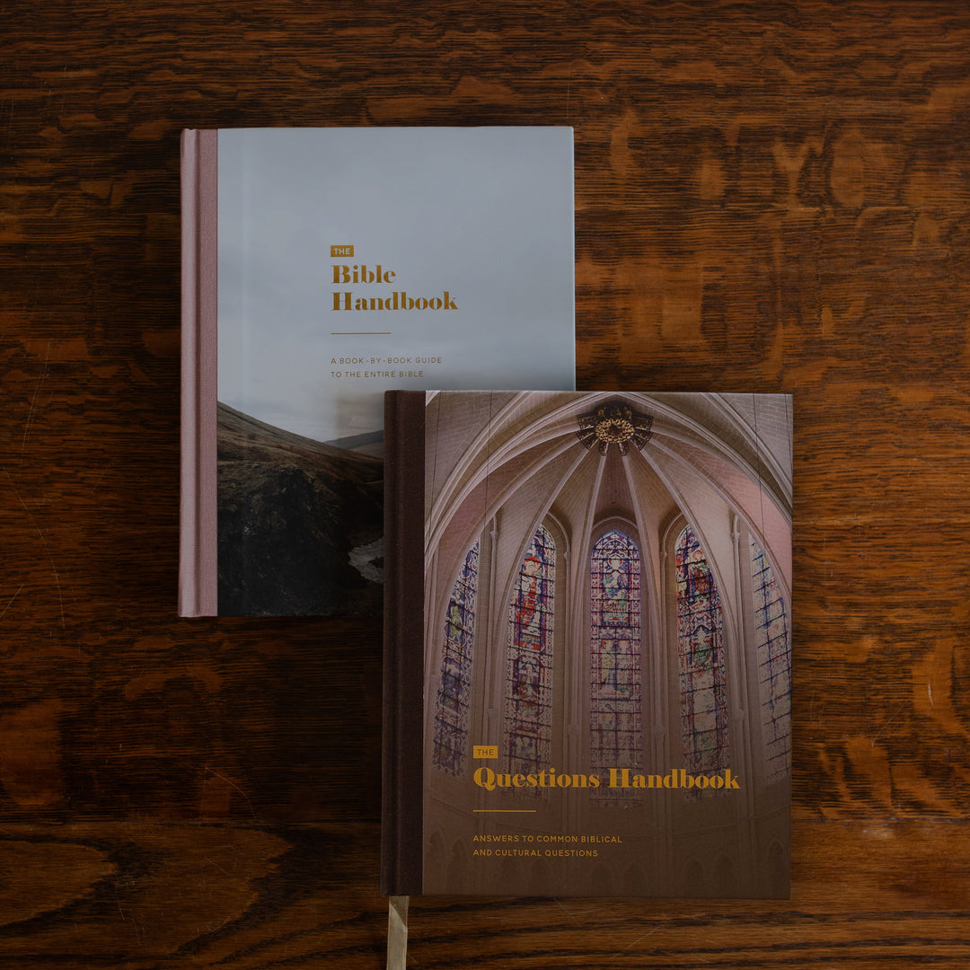 Two handbooks, 'The Bible Handbook' and 'Questions Handbook', arranged on a dark wood background.