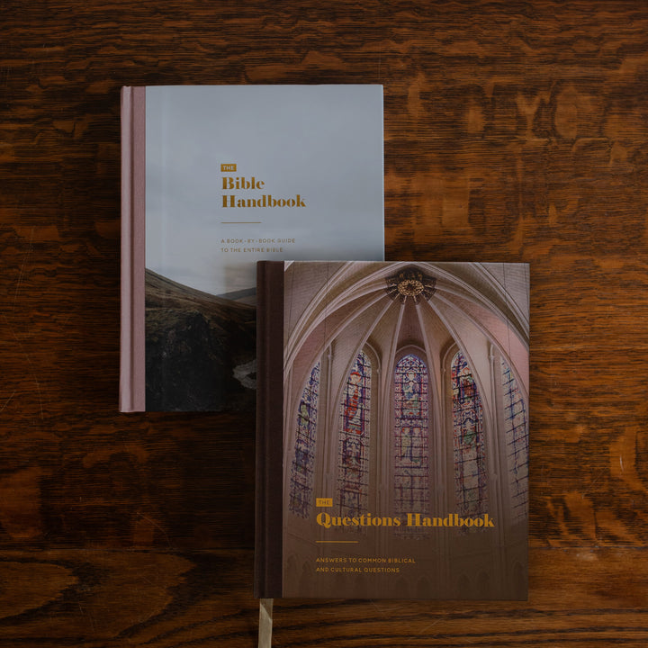 Two handbooks, 'The Bible Handbook' and 'Questions Handbook', arranged on a dark wood background.