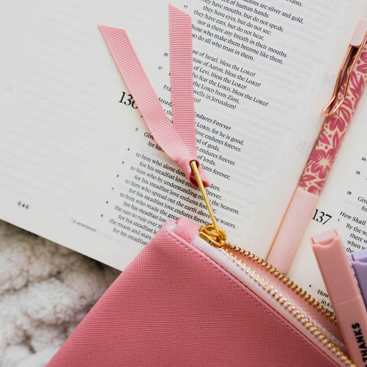 Renewed Day by Day Pencil Pouch - Blossom Pink on top of a Bible and a pen. 