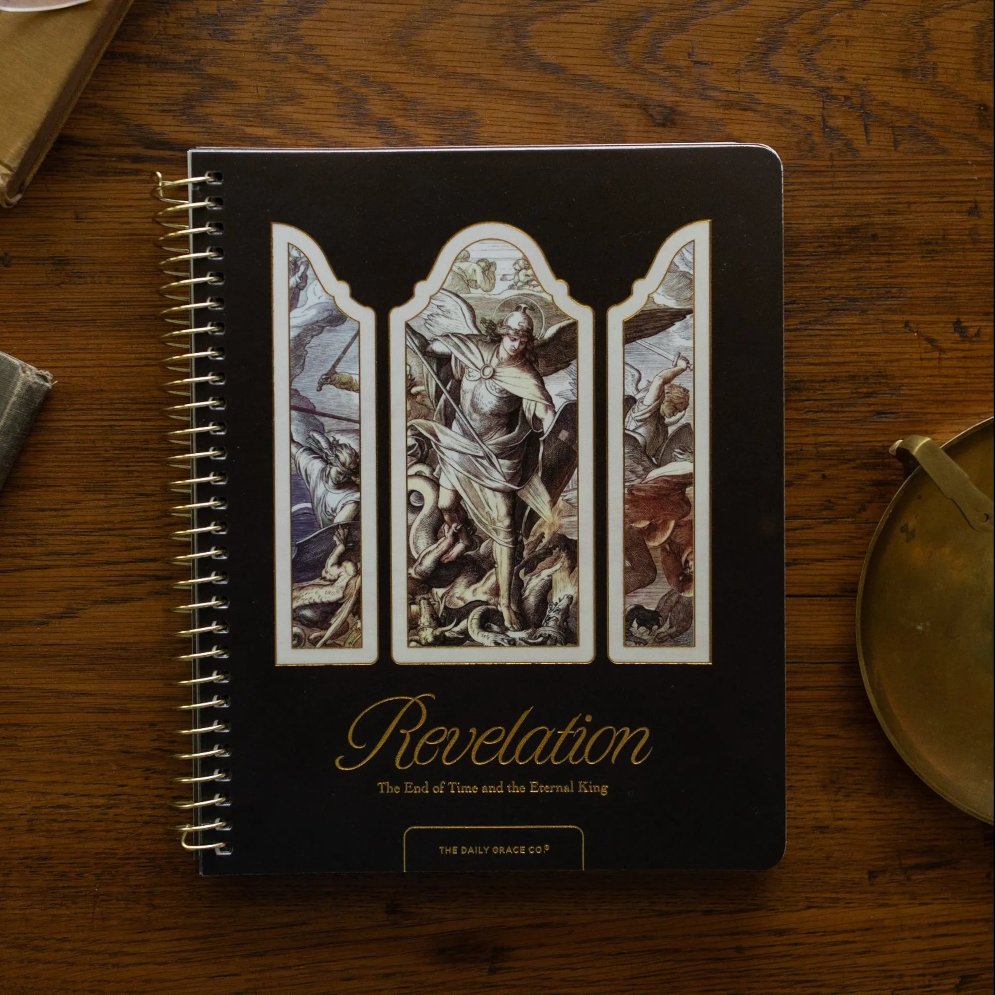 Revelation Spiral Study cover on a wooden table next to a bronze candlestick and some old books