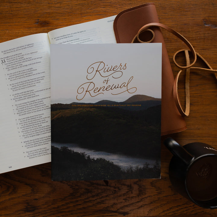 Rivers of Renewal Study cover laying on a open bible with a leather cover next to a coffee cup on a brown wooden table