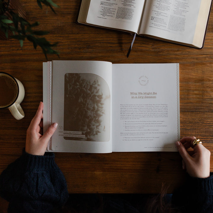 Rivers of Renewal Study opened to Why we might be in a dry season page with a woman holding the study open; There is a coffee cup next to the study and an open bible, resting on a brown wooden table