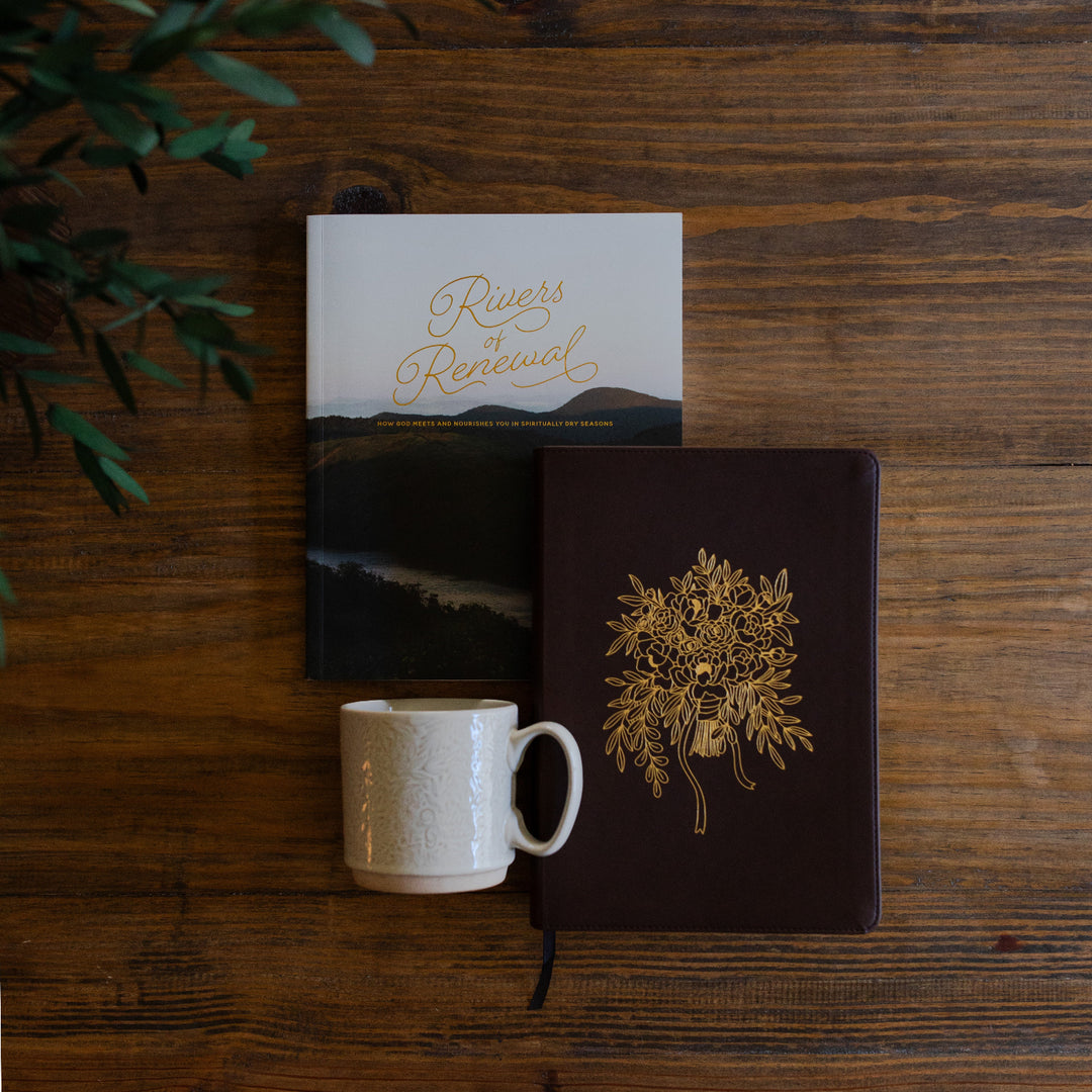 River of Renewal Woman's study cover next to a ESV Bible, Forever style, and a Daily Grace Mug laying on a brown wooden table with greenery in the corner