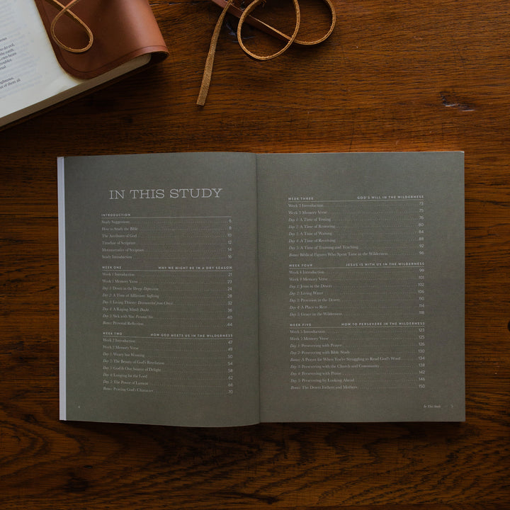 Rivers of Renewal Mens Study open to the table of contents page on a brown wooden table next to a leather wrapped bible