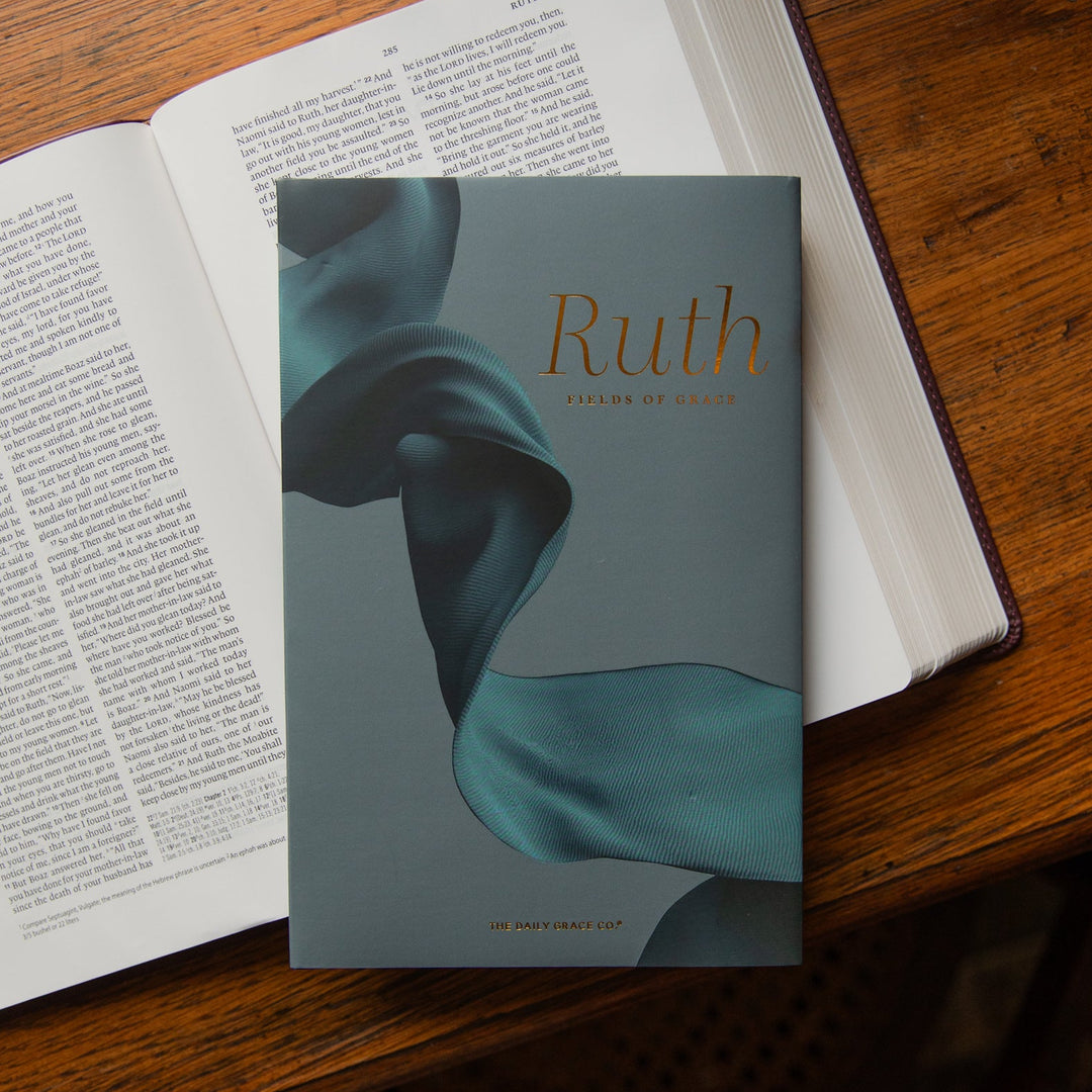 A book titled 'Ruth: Fields of Grace' by The Daily Grace Co rests on top of an open Bible on a wooden table.