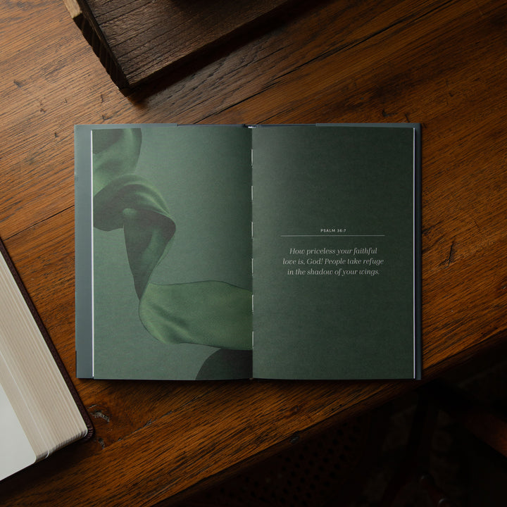 An open book laid flat on a wooden table, showing a green right page with small text and a green left page with a large image of a twisted ribbon.