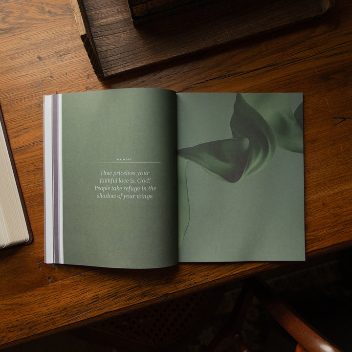 An open book lying on a wooden table, showing a two-page spread with a muted sage green design,  and a short quote on the left page.