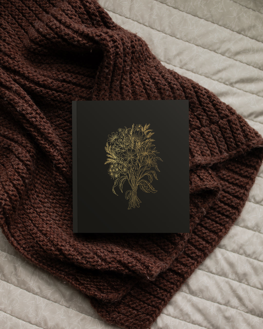 Dark book with gold embossed design on a brown knitted blanket