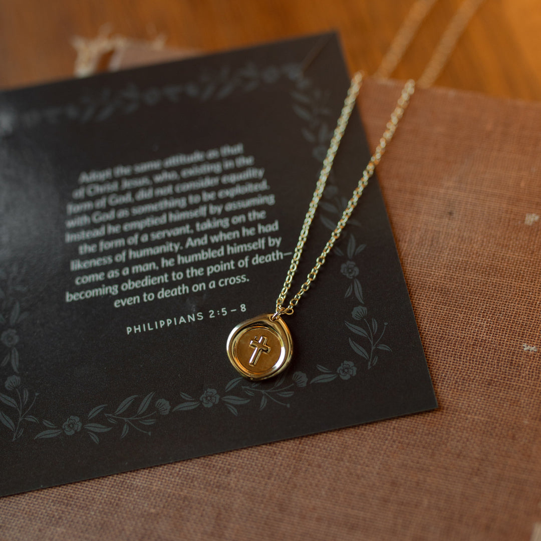 A sealed cross necklace on a verse card on a woven journal