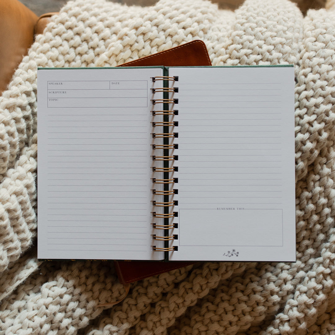 The Sermon Notes Journal with Green Floral opened to a blank page on a bible and a knitted blanket