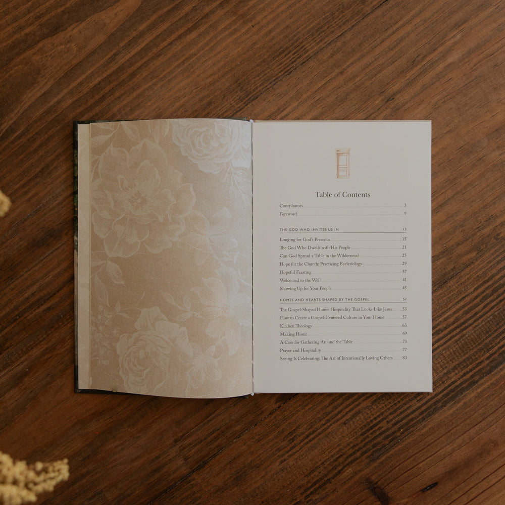 An open book laid flat on a wooden table, showing a printed table of contents page on the right and a floral-patterned left page. 