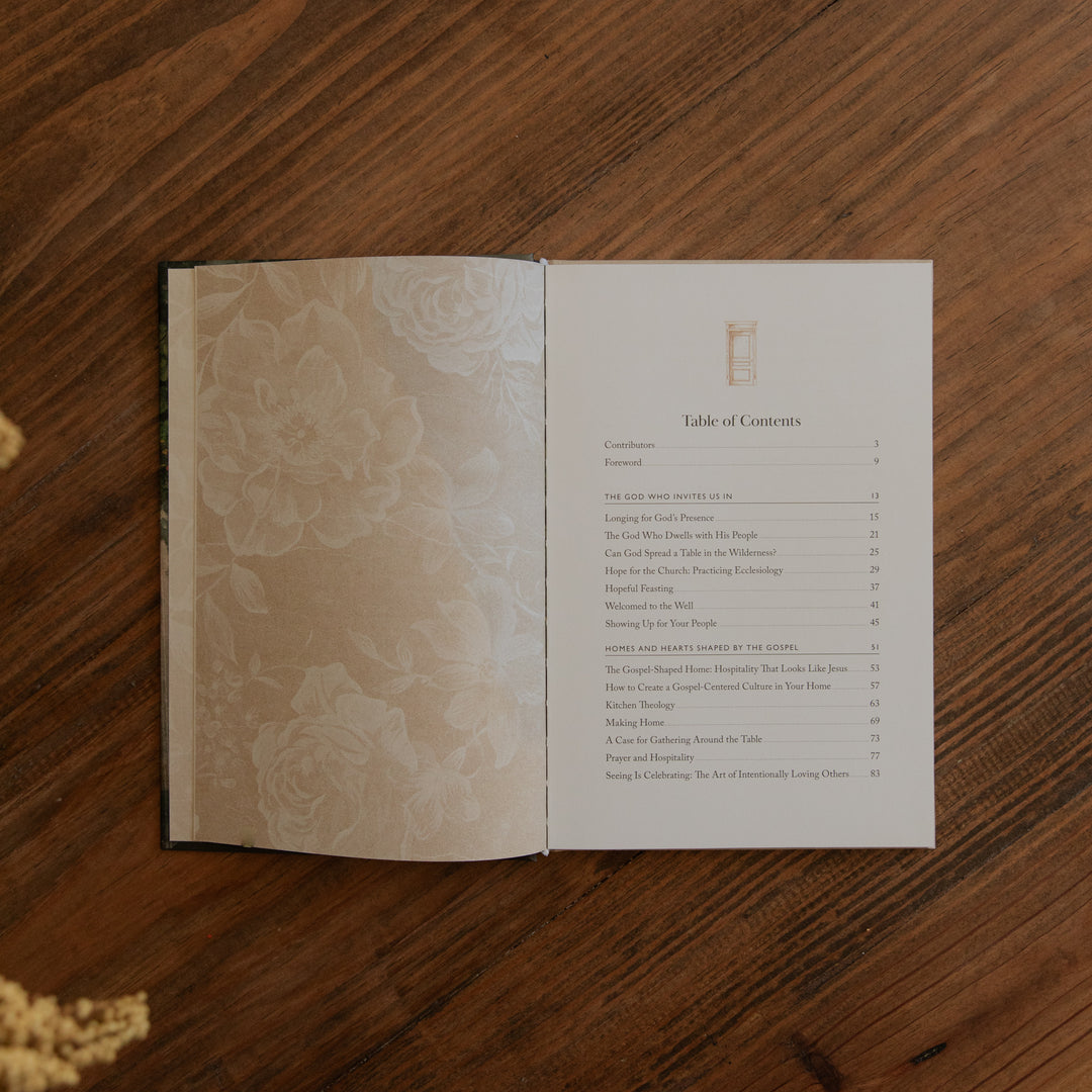 An open book laid flat on a wooden table, showing a printed table of contents page on the right and a floral-patterned left page. 