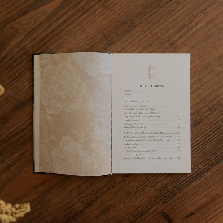 An open book laid flat on a wooden table, showing a printed table of contents page on the right and a floral-patterned left page. 
