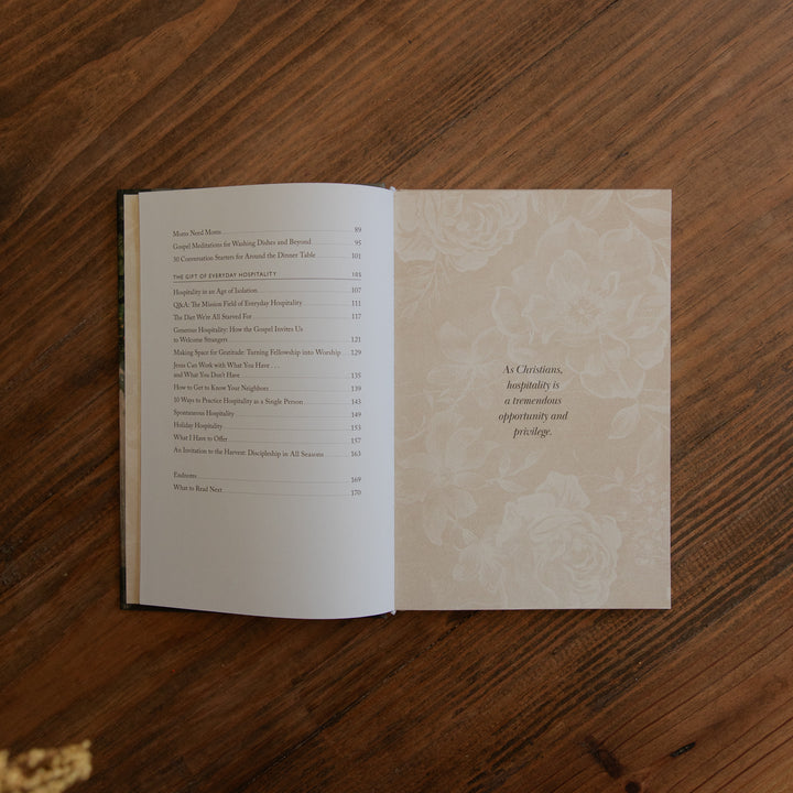 An open printed book laid flat on a wooden table, showing the left page with printed text and the right page with a decorative pale floral pattern and a quote.