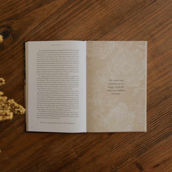 An open book with printed text on the left page and a decorative floral page on the right, placed on a wooden tabletop.