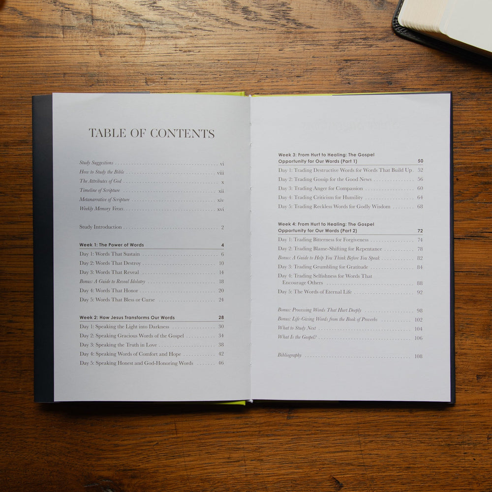 An open book showing the table of contents on a wooden tabletop, with another book partially visible in the top right corner.