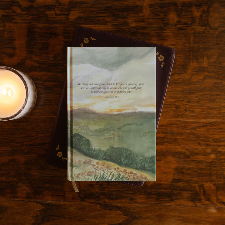 Strong and Courageous Lined Journal cover on a closed bible on a wooden table next to a lit candle