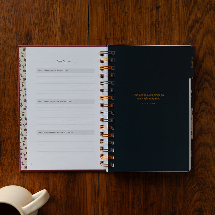 An open spiral-bound journal or planner lies on a wooden tabletop. The left page shows lined sections titled 'This Season.