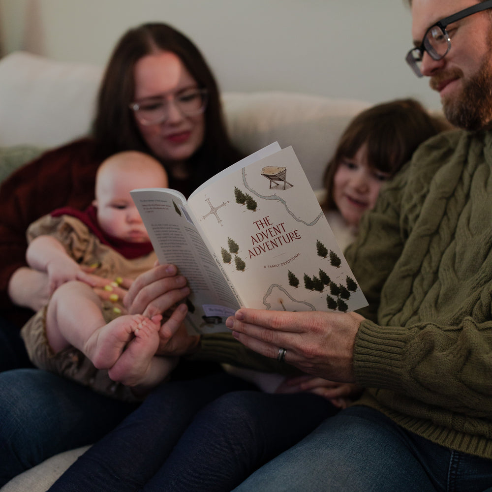 Four people sitting around on a couch while a man reads from The advent Adventure Devotional